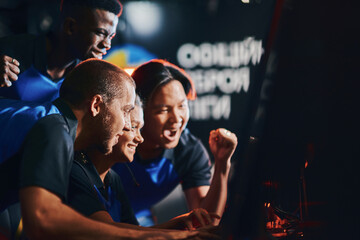Team of excited professional cybersport gamers looking at PC screen and celebrating success while participating in eSport tournament. Playing online video games - obrazy, fototapety, plakaty