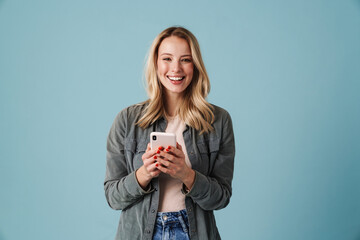 Cheerful beautiful blonde girl smiling and using mobile phone - obrazy, fototapety, plakaty