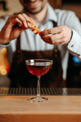 Bartender decorates alcoholic cocktail with orange peel