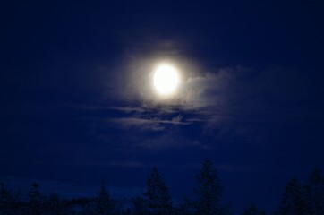 full moon on cold winter night sky over forest and field