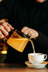 Male hands pour tea from a teapot into a cup