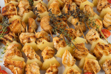 Chicken fillet kebab with pineapple on a white plate with tomatoes and thyme.