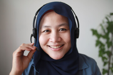 Beautiful Asian muslim woman using headphones speaking to camera, explaining something....