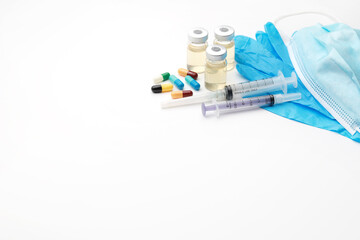 Close up image of medical syringe, vaccine vials, blue gloves, protective mask and antibiotics on white background. Copy space, soft focus image.