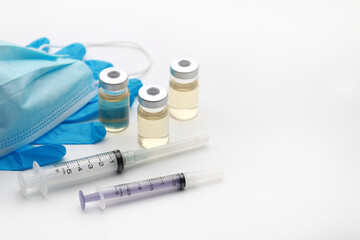 Close up image of medical syringe, vaccine vials, blue gloves, protective mask and antibiotics on white background. Copy space, soft focus image.