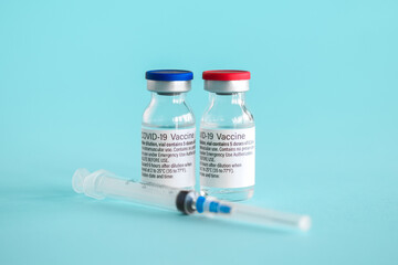 Ampoules with a vaccine against coronavirus infection COVID-19 and a syringe close-up on a light blue background