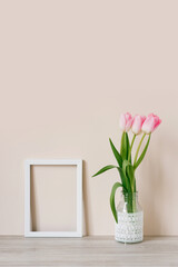 Home interior with decor elements. Mockup with a white frame and pink tulips in a vase on a light beige background