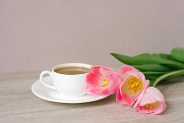 Obraz na płótnie Canvas Coffee with milk in a white porcelain cup and saucer, a bouquet of spring pink tulips. Mother's Day, Valentine's Day, Easter. The concept of spring
