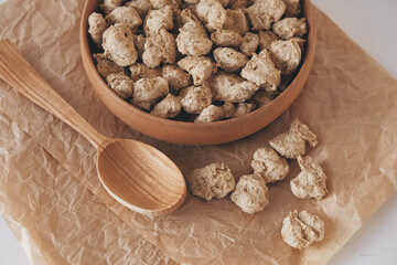 Raw dehydrated soy meat or dry soya chunks in wooden plate with a wooden spoon on white background. Top view. Copy, empty space for text