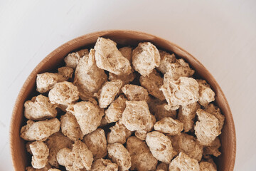 Raw dehydrated soy meat or dry soya chunks in wooden plate on white background. Top view. Copy, empty space for text