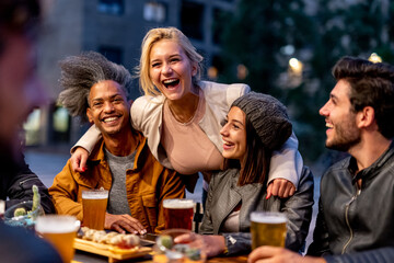 group of friends smiling and drinking at brewery, meeting of couple of millennials toasting with beers and eating fusion food, nightlife and social gathering of young people after covid19 outbreak