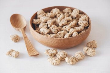 Raw dehydrated soy meat or dry soya chunks in wooden plate with a wooden spoon on white background. Top view. Copy, empty space for text