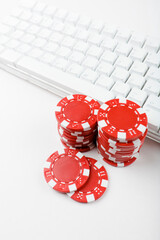 Piles of red poker chips next to a white keyboard. Gambling online concept.  Studio photo isolated on white background. Selective focus on object.