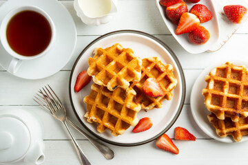 Delicious breakfast. Belgian waffles with honey and strawberries. Cup of tea white wooden background, top view.
