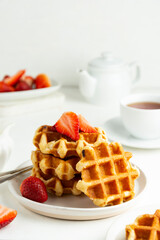 Delicious breakfast. Belgian waffles with honey and strawberries. Cup of tea white wooden background, top view.