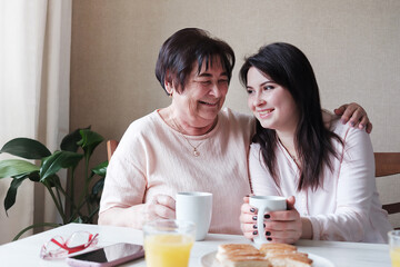 Grandmother lovingly hugs her daughter - Relatives are having fun at the table - Friends of a woman of different ages drink tea and chat - The concept of healthy family relationships