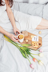 Fototapeta na wymiar Congratulations to your beloved woman on Valentine's Day. Breakfast in bed for a girl in a nightgown. Flowers and a gift for February 14