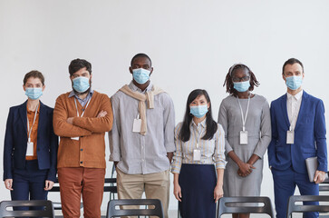 Multi-ethnic group of business people wearing masks and looking at camera while standing in row against white in conference room