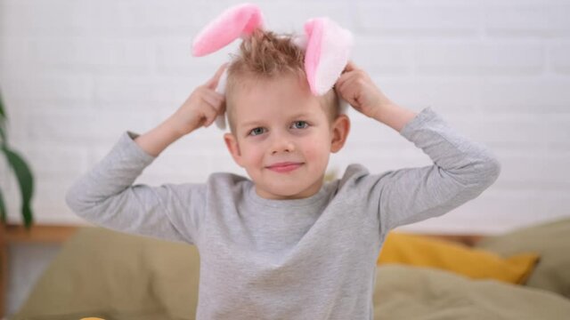 Portrait Easter kid. Boy putting on rabbit bunny ears on head having fun at home. Cheerful smiling child