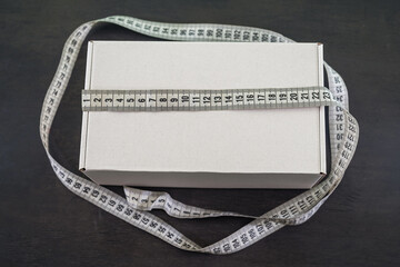 white cardboard box with measuring tape on black wooden background.