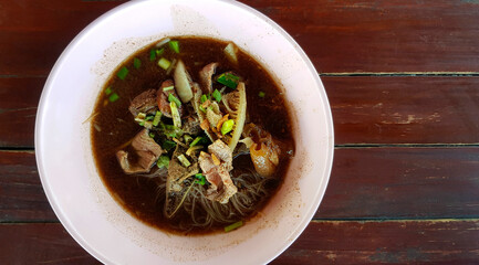 Top view of Thai rice noodle with beef, stale meat, liver, cow rag, offal and on brown wooden background or table and copy space on right at local street food. Flat lay of Asian food on pink bowl.