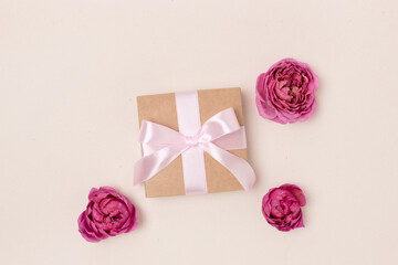 Gift box with a tied ribbon and heads of rose flower on a beige background. Present for a Mothers Day or 8 March.