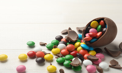 Broken chocolate egg and colorful candies on white table. Space for text