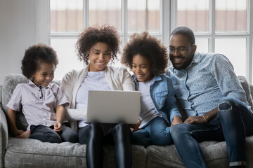 Close up happy African American family with kids using laptop, smiling mother and father with adorable little daughter and son looking at computer screen, shopping online, video call, leisure time