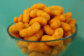 peanut flips . close up lots of corn sticks in a peanut butter glaze in a glass round bowl on a light blue background side view . high-calorie snack