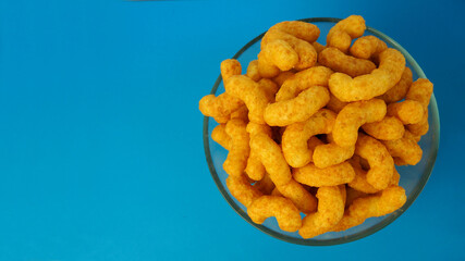 peanut flips . lots of corn sticks in a peanut butter glaze in a glass round bowl on a blue background top view . high-calorie snack