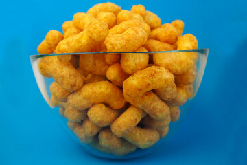 peanut flips . lots of corn sticks in a peanut butter glaze in a glass round bowl on a blue background side view