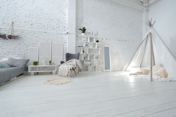 Spacious stylish modern trendy loft apartment in white and light colors. brick wall, wood floor, shelving, pallet bed and teepee-shaped children's house. everything is white with gray tints.
