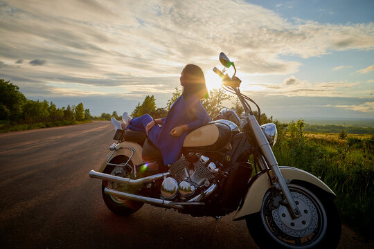 Attractive brunette motorcyclist with motorcycle in a summer evening during sunset. Adventure and travel concept.