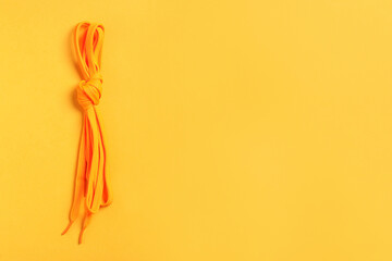 Orange shoelaces on yellow background, top view. Space for text