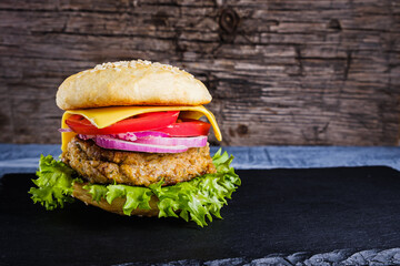 Fresh delicious homemade veggie burger lies on natural slate on rustic wooden background. Delicious tasty burger with lettuce, cheese, onion and tomato. buckwheat and lentil cutlet