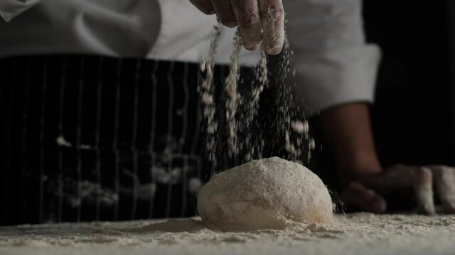 Slow Motion shot of  bakery chef applying and sprinkles flour over bread dough. Baking concept.