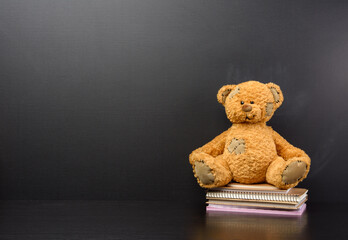 brown teddy bear sits on a brown wooden table, behind an empty black chalk board, back to school