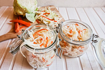 Homemade sauerkraut with carrots in two glass jars on a white wooden table.  Fermented vegetables. Vegetarian vegan food. Sauercraut- cut, fermented cabbage, german and russian style cuisine.