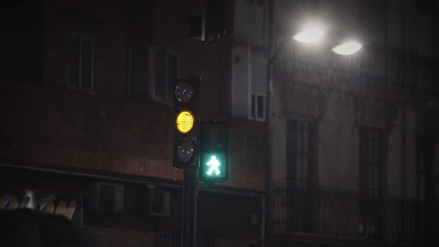 Green traffic lights and people with umbrellas hurrying to cross the street. View at rainy night