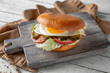 Tasty grilled burger with beef, bacon, fried egg, cheese, vegetables. Delicious grilled gourmet hamburger on a dark background. Free space for text