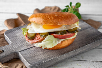 Tasty grilled burger with beef, bacon, fried egg, cheese, vegetables. Delicious grilled gourmet hamburger on a dark background. Free space for text