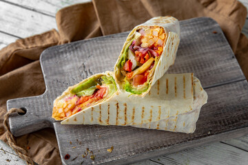 A delicious doner donair kebab wrap with meat, french fries, lettuce, tomato,  onion and sauce.
