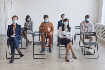 Full length multi-ethnic group of business people wearing masks and social distancing while sitting...