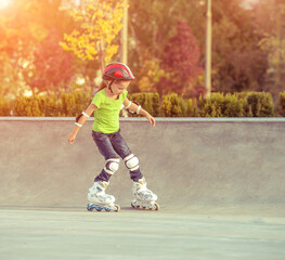 Little girl on roller skates in helmet at a park at sunset