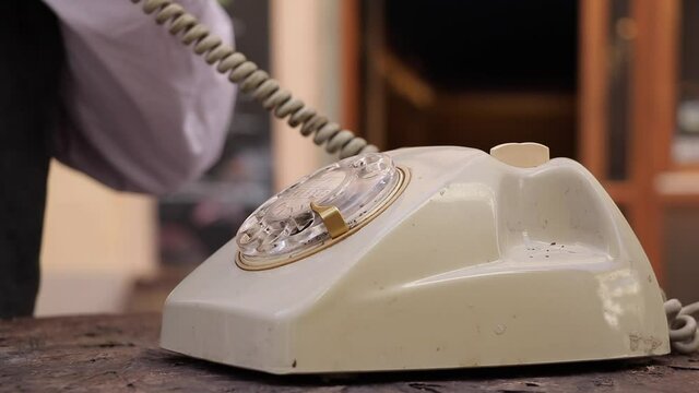 Close-up view of a hand picking up the telephone receiver and dialing two numbers on an old rotary phone.