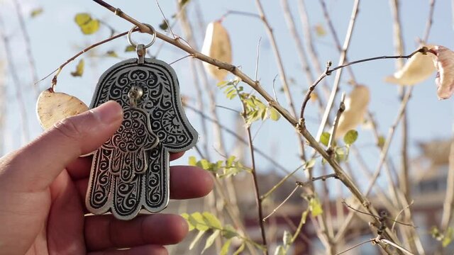 A person gently touches the symbol of the hand of Fatima on a tree branch.