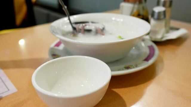 A woman serving congee with preserved egg and meat for a friend inside a Chinese restaurant with 4k resolution.