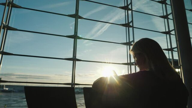 Business lady uses a smartphone at the airport. Silhouette, look from the back