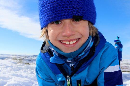 Ni&ntilde;o rubio con ojos verdes sonriendo en la nieve con el cielo azul