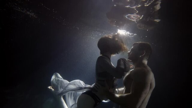 sexy lady and brawny man are embracing underwater against sunlight through surface